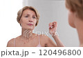 Beautiful woman in her 40s critically examines her appearance in the mirror, upset and anxious about skin imperfections and wrinkles. Slo mo 120496800