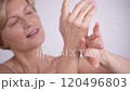 Positive blond woman in her 50s applying hand cream. Charming lady gently massaging her hands, enjoying anti-aging skincare rituals at home 120496803