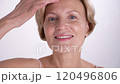 Beautiful woman in her 50s gently touches her radiant face and neck, enjoying her reflection in the mirror. Skincare for aging skin. 120496806