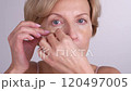 A middleaged female looking into the mirror, applying eye patches and smiling. Gracefully aging female takes care of her skin and beauty 120497005