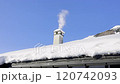 Picturesque winter landscape featuring a chimney emitting smoke on a snow-covered roof under a bright blue sky, the surrounding snow-draped landscape and clear weather  serene and peaceful atmosphere  120742093