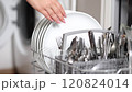 Close-up view of human hand removing clean plates from a loaded dishwasher. Background of open wash machine  120824014