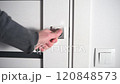 Man opening modern white door with metallic handle 120848573