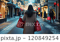 Woman walking down snowy street carrying shopping bags during christmas time 120849254