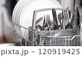 Female hand put dirty cutlery to dishwasher. Plate in dishwasher. Background of open wash machine  120919425