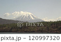 Snow-capped Mount Fuji towering over a lake and forest in the foreground, fixed shot 120997320