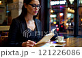 A beautiful woman wearing glasses is reading her notebook in a cafe 121226086