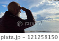 A man with a gray beard in a jacket stands against the background of the sea 121258150