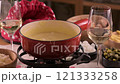 Cozy Swiss fondue setup with melted cheese, bread, pickles, and wine on a rustic table. advertising 121333258