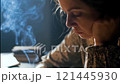 Woman reads a book in a dimly lit room, surrounded by rising smoke from an unseen source. The atmosphere conveys a sense of concentration mixed with concern over secondhand smoke 121445930
