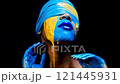 Woman posing with blue and yellow paint on her face, eyes covered by a blue cloth, showcases artistic expression against a striking black background 121445931