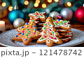 Decorated gingerbread cookies shaped like Christmas trees and stars on a plate, surrounded by festive lights and holiday ornaments 121478742