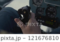 A pilot's hand adjusts the control stick in a cockpit as flight instruments display crucial information. 121676810