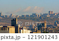 A time-lapse video of an urban landscape during the day, with moving clouds, small cars. Against a backdrop of buildings, a hill, blue sky and trees. 121901243