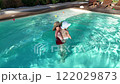 Mother holding baby in outdoor swimming pool enjoying a warm sunny day together 122029873