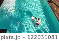 Mother playing with baby in outdoor swimming pool surrounded by nature on a sunny day 122031081