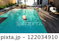 Mother and baby enjoying playtime in outdoor swimming pool surrounded by greenery on a sunny day 122034910