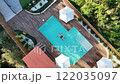 Aerial view of man floating in luxurious backyard swimming pool with wooden deck and umbrellas 122035097