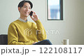 Young man sitting on sofa and talking on smartphone 122108117