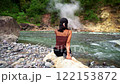 Asian girl sitting on a rock on the bank of a strong mountain river looking at geothermal spring and green jungle 122153872