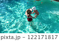 Mother and baby enjoying playtime in outdoor swimming pool surrounded by greenery on a sunny day 122171817
