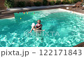Mother and baby enjoying playtime in outdoor swimming pool surrounded by greenery on a sunny day 122171843