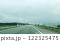 Highway stretching through the countryside with fields and trees under an overcast sky. Calm landscape, empty asphalt road, scenic horizon, and a peaceful journey in motion. 122325475
