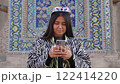 Uzbek woman in a stunning headdress uses her smartphone, merging ancient traditions with a digital lifestyle 122414220