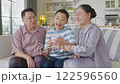 Asian Cheerful boy enjoying milk with loving grandparents on cozy sofa in bright living room, sharing happiness, love, and family bonding moments of togetherness. 122596560