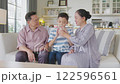 Asian Cheerful boy enjoying milk with loving grandparents on cozy sofa in bright living room, sharing happiness, love, and family bonding moments of togetherness. 122596561