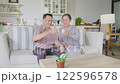Asian Elderly couple sitting on cozy sofa in bright living room, smiling and enjoying glasses of milk together, creating warm atmosphere of happiness, bonding, and togetherness at home. 122596578