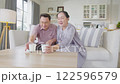 Asian Elderly couple relaxing together on white sofa in bright living room, drinking milk and enjoying peaceful moments at home, creating warm and cozy atmosphere. 122596579