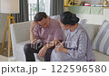 Asian Elderly Woman Comforts Elderly Man with Headache on Sofa in Cozy Living Room, Offering Support and Care at Home for Pain Relief 122596580