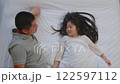 Joyful father and daughter lying together on bed, sharing happy conversation. Father gently touches his daughter face creating moment of warmth and connection. Both appear relaxed and smiling 122597112