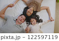 Asian joyful family scene featuring afather, mother, and their young daughter lying comfortably on a bed. The family is enjoying a peaceful and intimate moment, with the child pointing excitedly 122597119