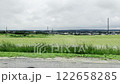 View from a car of rolling hills and vast green fields with crops, a rural village, houses, and church steeples under a cloudy, overcast sky. Scenic, serene, and peaceful pastoral landscape. 122658285