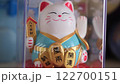A smiling Maneki Neko figurine in a blue outfit, holding a golden plaque with Chinese characters, meaning wealth comes from all directions, good fortune and attracting good things and happiness. 122700151