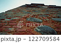 Weathered brick wall rising against a clear sky 122709584