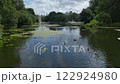 A tranquil pond in Public Park with lush greenery in the foreground, while the Iconic landmark and surrounding buildings are visible in the background.  122924980