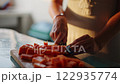 Close up of woman's hands cutting papaya fruit, pawpaw fruit in half using a knife. Female cook preparing papaya, chef in a brightly lit kitchen.  122935774