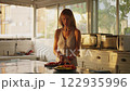 Open kitchen and woman's hands cutting papaya fruit, pawpaw fruit in half using a knife. Female cook preparing papaya, chef in a brightly lit kitchen.  122935996