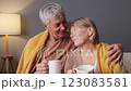 A loving couple sits closely together wrapped in soft blankets, sharing warm drinks and enjoying each other's company in a comfortable living room during the evening 123083581