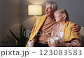 A couple sits together on a couch, enjoying comfort beverages while wrapped in warm blankets. The atmosphere is cozy, with soft lighting providing a relaxed vibe in their living room 123083583