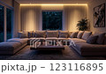 A spacious living room at dusk features a large, plush sectional sofa as the centerpiece, illuminated by warm overhead and accent lighting, with large windows offering a view into the forest 123116895