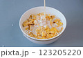 A close-up of fresh milk being poured into a bowl of golden cornflakes 123205220