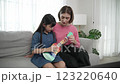 Happy girl playing ukulele while caucasian mom teaching and explain. Pedagogy. 123220640