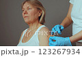 An elderly woman sits calmly as a healthcare professional administers a vaccination. The setting is clean and well-lit, highlighting the importance of inoculation for health 123267934