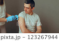 A healthcare professional in gloves administers a vaccination to a seated man who is prepared for the inoculation. The setting is well-lit and sterile, promoting a sense of safety and health 123267944