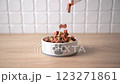Pouring dry dog food in a shape of bones in bowl on wooden floor background. Plate full of mineral healthy dog food closeup. Pet snack in white bowl. 123271861