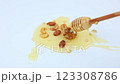 Walnuts and pine nuts, almonds and cashews lie on a white background in a puddle of yellow liquid honey, honey drips from a wooden spoon on top of them, it is lowered and placed next to it. The 123308786